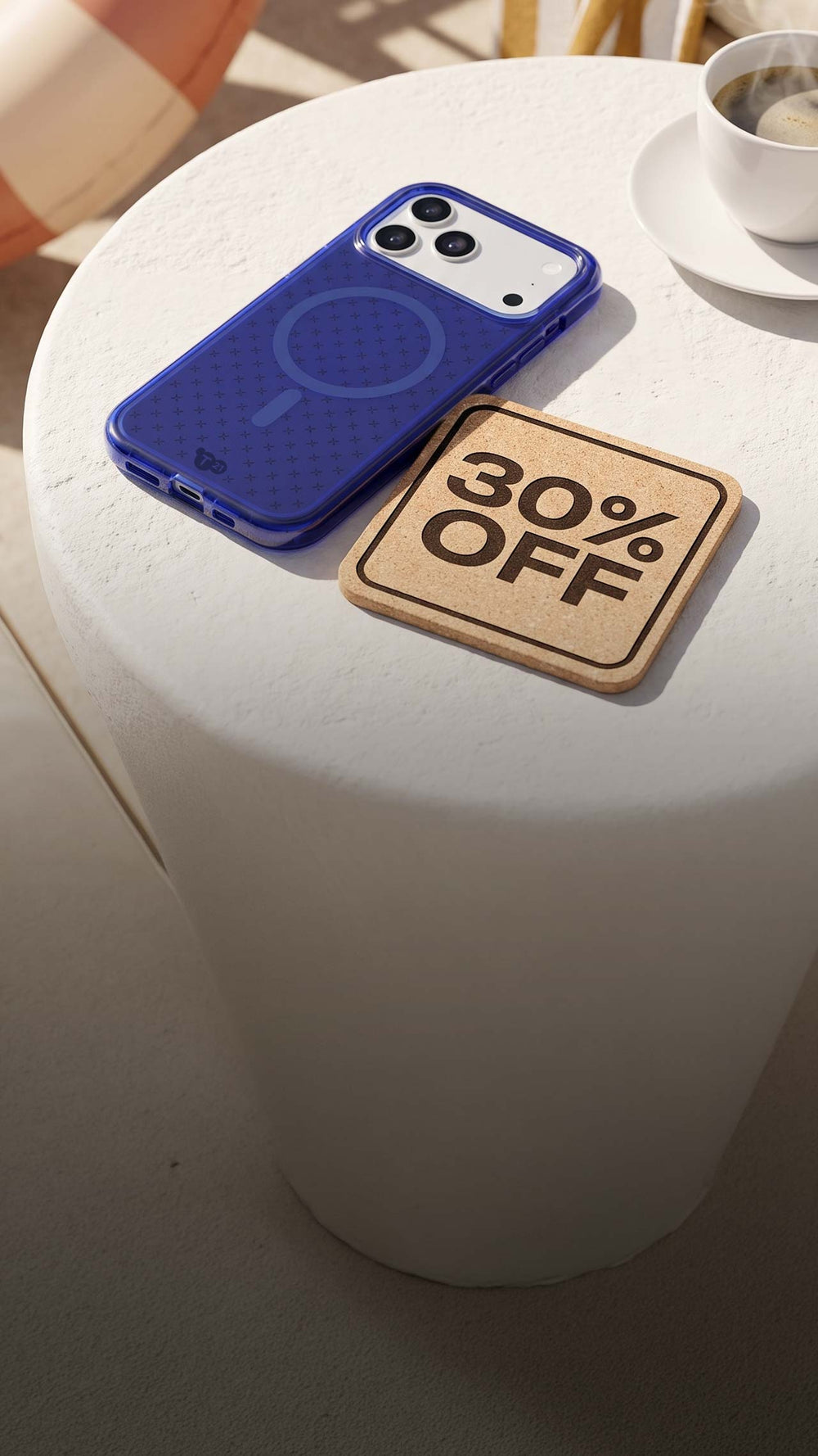 An iPhone in blue Tech21 case sits on a table next to a steaming up of coffee with a coaster next to it that reads: 30% OFF